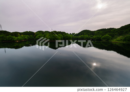 The sun gradually sinks under a slightly cloudy sky and the sun is reflected on the lake surface moving symmetrically at Nunome Dam in Nara City ⑧ 126464927
