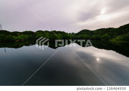 The sun gradually sinks under a slightly cloudy sky and the sun is reflected on the lake surface in a symmetrical motion at Nunome Dam in Nara City⑪ 126464930