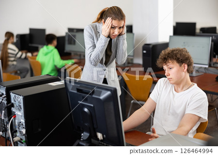 Frustrated teacher talking to neglectful teenage student in computer class Frustrated teacher talking to neglectful teenage student in computer class 126464994