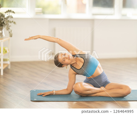 Sportive girl practicing seated side bend pose of yoga in light room Sportive girl practicing seated side bend pose of yoga in light room 126464995
