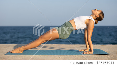 Positive girl practicing reverse plank pose of yoga on seashore 126465053
