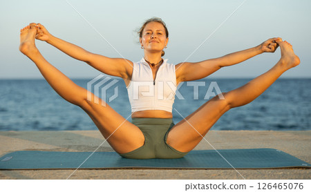 Girl practicing hatha yoga on sea beach, stretching in an asymmetrical seated asana Parivritta Janu Sirsasana Girl practicing hatha yoga on sea beach, stretching in an asymmetrical seated asana Parivritta Janu Sirsasana 126465076
