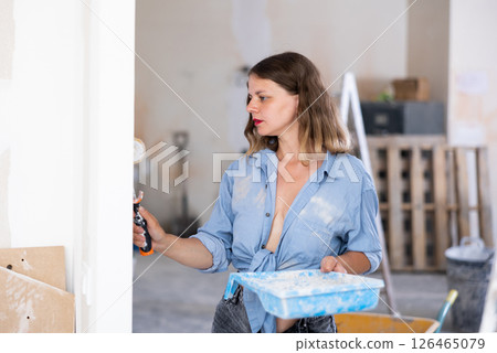 Casual young woman painting walls with a paint roller in refurbished room 126465079