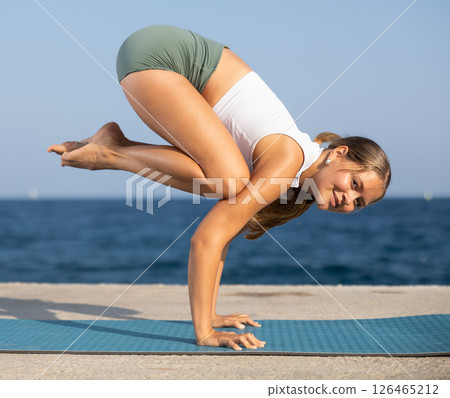 On windy day young slender woman does yoga near sea doing bakasana On windy day young slender woman does yoga near sea doing bakasana 126465212