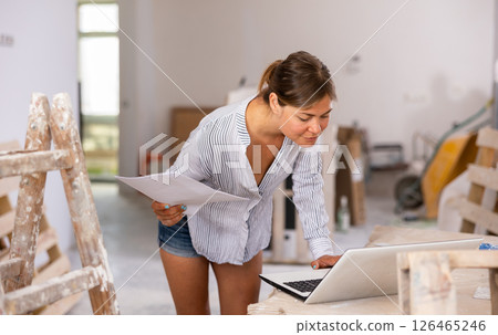 Female designer working with laptop and papers in apartment under renovation Female designer working with laptop and papers in apartment under renovation 126465246
