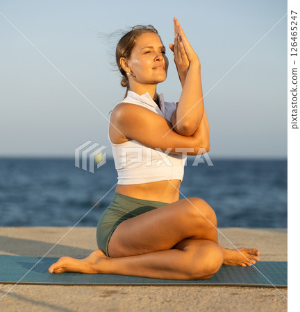Sportive girl practicing eagle pose of yoga on seashore Sportive girl practicing eagle pose of yoga on seashore 126465247