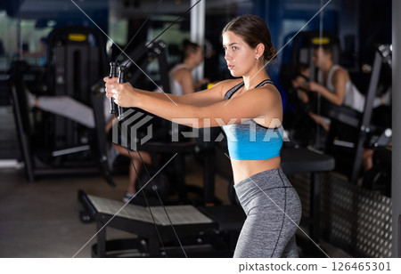 Active athlete young woman during exercises on crossover exercise machine with loops and weighting 126465301