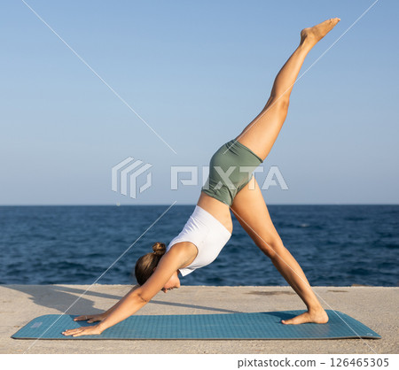Sportive girl practicing downward dog pose of yoga on seashore Sportive girl practicing downward dog pose of yoga on seashore 126465305