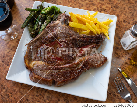 Grilled beef chop on bone, served with a vegetable side dish of fried potatoes and green padron peppers Grilled beef chop on bone, served with a vegetable side dish of fried potatoes and green padron peppers 126465306