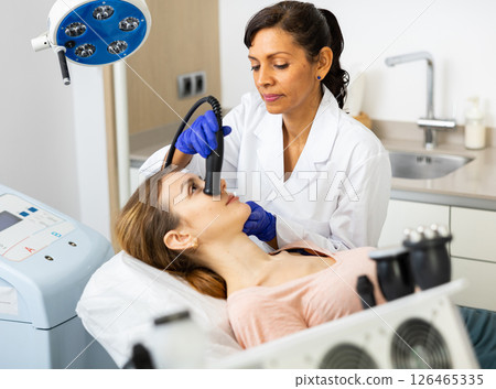 Hispanic woman beautician doing needle-free mesotherapy for young woman Hispanic woman beautician doing needle-free mesotherapy for young woman 126465335