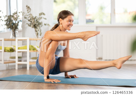Sportive girl practicing complex pose of yoga in light room Sportive girl practicing complex pose of yoga in light room 126465336