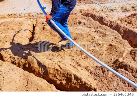 Electrician man works diligently, laying electrical PVC pipe in trench at construction site hardworking outdoor setting. 126465346