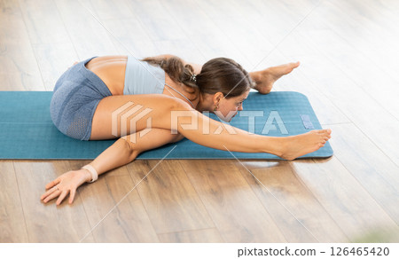 Slender positive girl performs various yoga poses in bright room 126465420