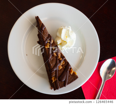 Sweet tender piece of chocolate-nut pie decorated with ball of cream ice cream is served on plate 126465446