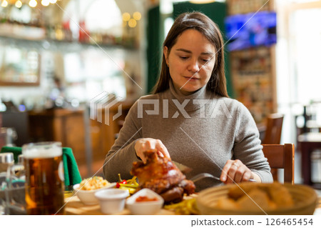 Positive brunette having lunch in cafe with roasted ham hock and beer Positive brunette having lunch in cafe with roasted ham hock and beer 126465454