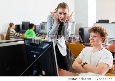 Frustrated teacher talking to neglectful teenage student in computer class Frustrated teacher talking to neglectful teenage student in computer class 126465467