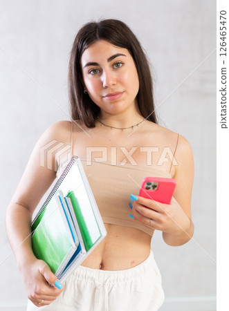 Young woman posing with notebooks and mobile phone against wall 126465470