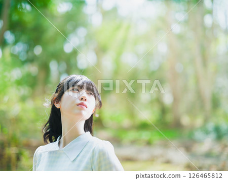 一位年輕的日本女性在一片新綠色的森林裡沐浴陽光 一位年輕的日本女性在一片新綠色的森林裡沐浴陽光 126465812