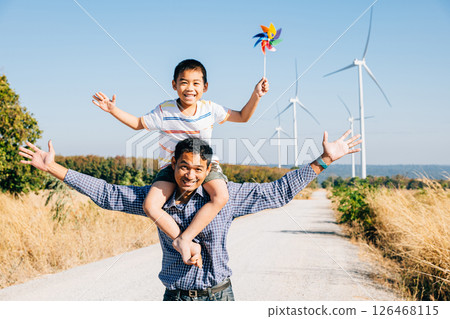 Dad smiles while carrying daughter with pinwheel. Family joy near windmills signifies global innovation in renewable energy. A moment of bonding and happiness in the community. Father Day Dad smiles while carrying daughter with pinwheel. Family joy near windmills signifies global innovation in renewable energy. A moment of bonding and happiness in the community. Father Day 126468115
