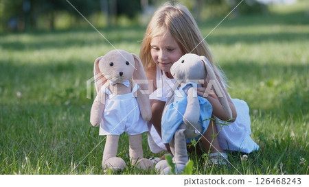 Child engages in a playful activity with plush bunnies, surrounded by green grass and sunshine, embodying innocence and creativity on a lovely day. 126468243