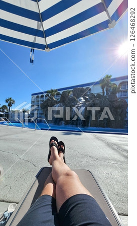 Relaxing Vacation by the Pool Man Lounging Under Umbrella with Waterfall View. Sunny Day Relaxing Vacation by the Pool Man Lounging Under Umbrella with Waterfall View. Sunny Day 126468292