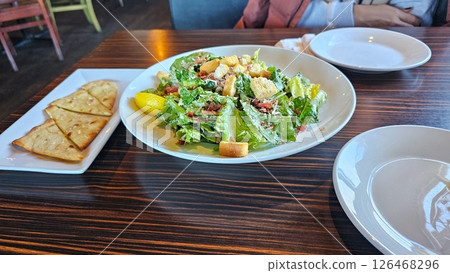 Fresh Caesar Salad on a Wood Table with Plates and Crispbread, Restaurant Setting Fresh Caesar Salad on a Wood Table with Plates and Crispbread, Restaurant Setting 126468296