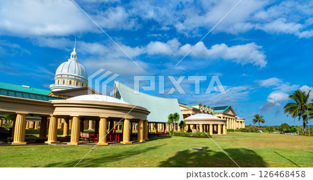 Panoramic view of the Palau National Capitol complex in Ngerulmud, Melekeok State, with its dome, columns, and distinctive rooflines framed by palm trees and blue skies 126468458
