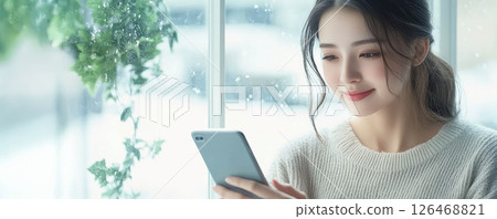 A woman enjoys her phone while sitting by the window in a cozy atmosphere. A woman enjoys her phone while sitting by the window in a cozy atmosphere. 126468821