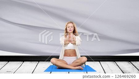 Image of caucasian woman in lotus position practicing yoga meditation over blowing grey fabric 126469260