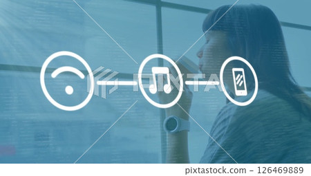 Image of media icons over biracial businesswoman drinking coffee in office 126469889