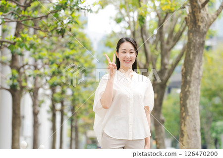A woman smiling and making a peace sign in the city A woman smiling and making a peace sign in the city 126470200