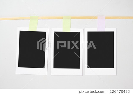Three blank polaroid photo papers with sticky tape hanging on the rope with a white background. Mockup, template, or copy space. Instant camera photo print frame 126470453