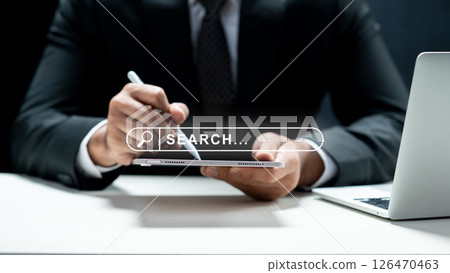 Businessman using a tablet and showing a search engine bar icon on the screen. Laptop on the desk. Technology innovation on the virtual screen. Concept of technology and web network Businessman using a tablet and showing a search engine bar icon on the screen. Laptop on the desk. Technology innovation on the virtual screen. Concept of technology and web network 126470463