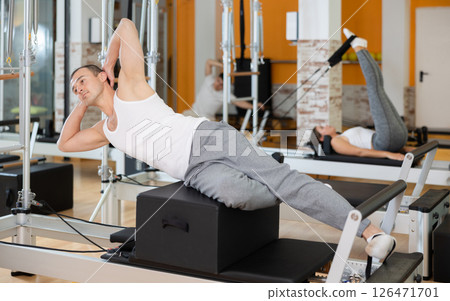 Man in different poses performs static and dynamic exercises on reformer Man in different poses performs static and dynamic exercises on reformer 126471701