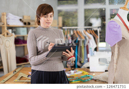 Female fashion designer drawing clothing on tablet in studio Female fashion designer drawing clothing on tablet in studio 126471731