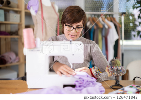Female clothing designer stitching fabric on sewing machine in studio 126471842