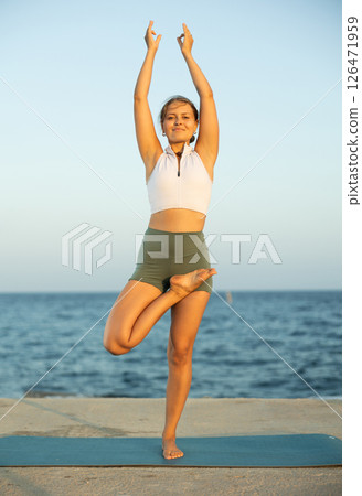 Sportive girl practicing tree pose of yoga on seashore 126471959