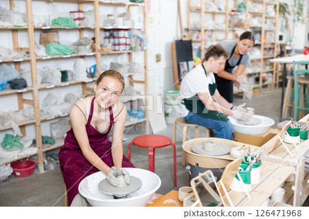 Young woman teacher helps teenagers boy and girl to make product on potter's wheel 126471968