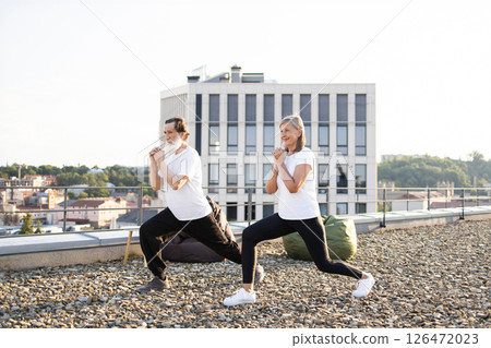 Elderly couple practicing yoga stretches on rooftop during sunny morning, promoting health, mindfulness. Elderly couple practicing yoga stretches on rooftop during sunny morning, promoting health, mindfulness. 126472023