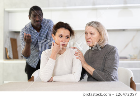 Old woman trying to calm angry middle-aged woman while man quarreling to her Old woman trying to calm angry middle-aged woman while man quarreling to her 126472057