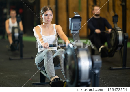 Girl exercising on rowing machine during intense full body workout 126472254