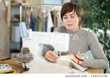 Working in sewing workshop - female dressmaker working at sewing machine making stitches on fabric 126472256