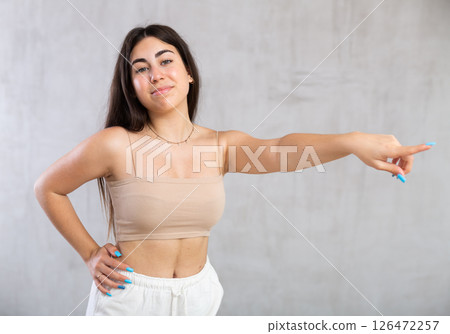 Young woman pointing aside standing against the wall Young woman pointing aside standing against the wall 126472257