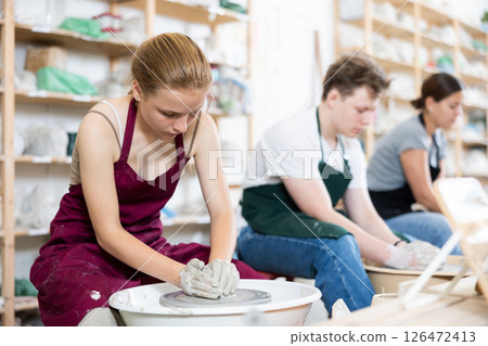 Young woman teacher and two teenagers make products on potter's wheel Young woman teacher and two teenagers make products on potter's wheel 126472413
