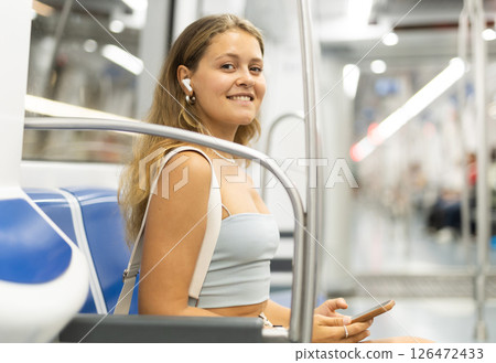 Young woman is sitting in subway car with headphones and phone, getting to work Young woman is sitting in subway car with headphones and phone, getting to work 126472433