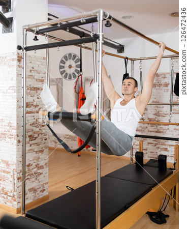 Man performing hanging exercise on cadillac table in Pilates studio 126472436