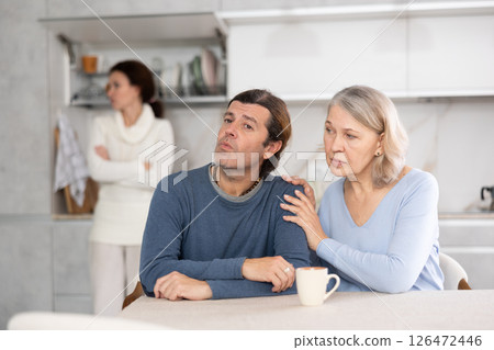 Senior woman sits near adult son and comforts him during quarrel with wife. Senior woman sits near adult son and comforts him during quarrel with wife. 126472446