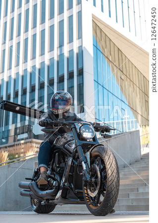 Handsome motorcyclist with helmet sitting on his moto against urban backdrop Handsome motorcyclist with helmet sitting on his moto against urban backdrop 126472450