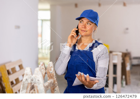 Female worker in blue overall discussing repair plan on mobile phone Female worker in blue overall discussing repair plan on mobile phone 126472479
