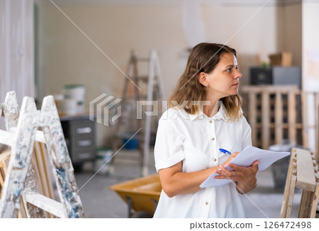 Female architect matching check list during repair works Female architect matching check list during repair works 126472498